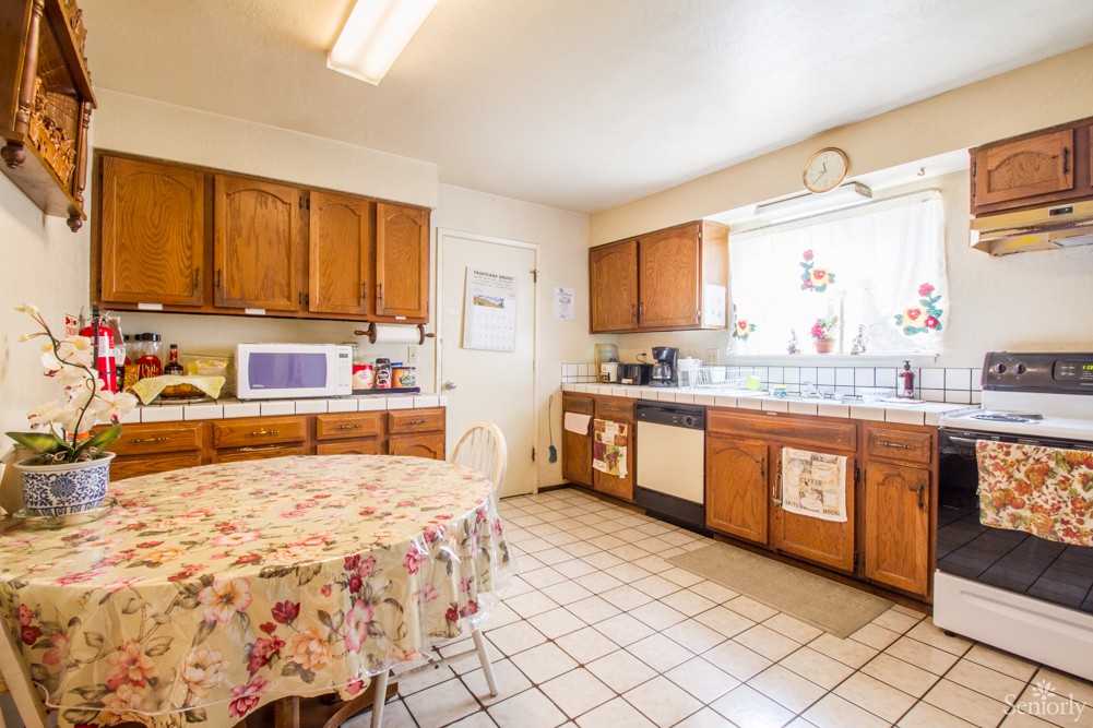 A bright kitchen with wooden cabinets and a dining table, featuring a microwave and various appliances.