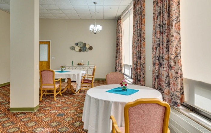 A well-furnished dining room with round tables, cushioned chairs, and decorative elements.