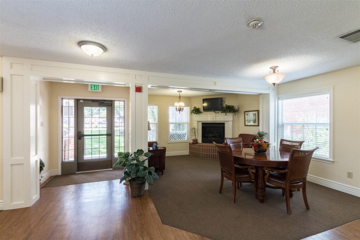 A cozy living room with a fireplace, table, and chairs surrounded by large windows.