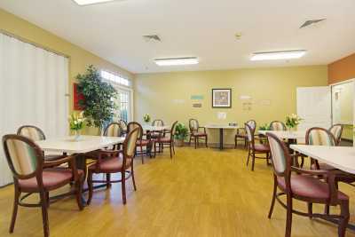 A spacious dining room with several empty tables and chairs, decorated with plants and artwork.