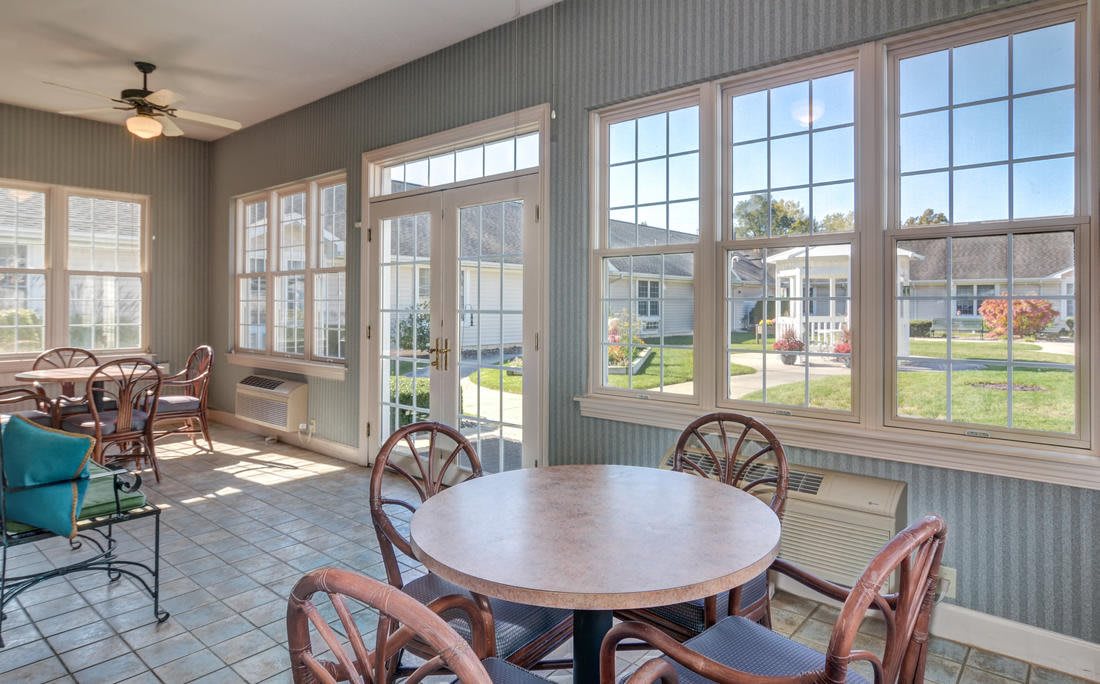 A bright sunroom with a circular table and chairs, featuring large windows letting in natural light.