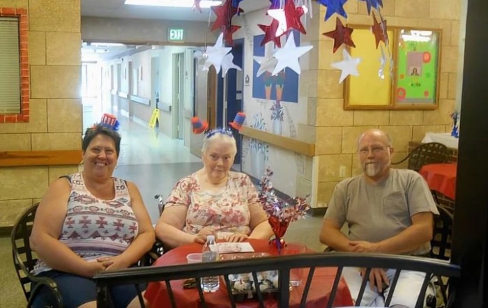 Three people sitting at a decorated table with patriotic-themed decorations in a hallway.