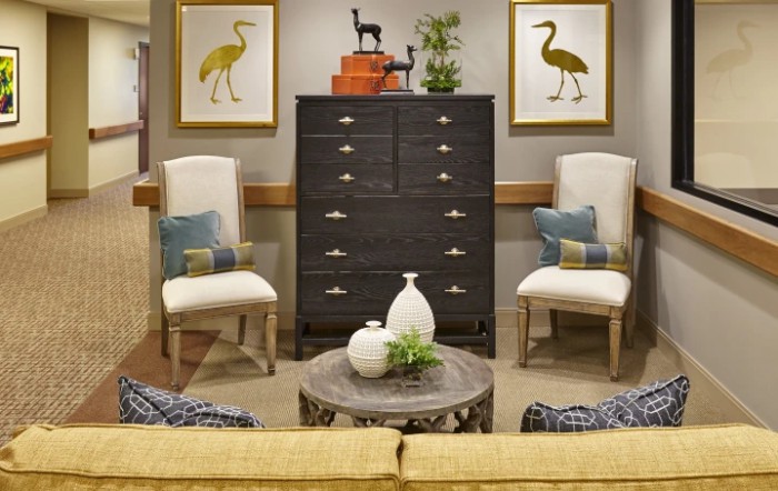 A cozy living room featuring a black dresser, two elegant chairs, and colorful artwork on the walls.