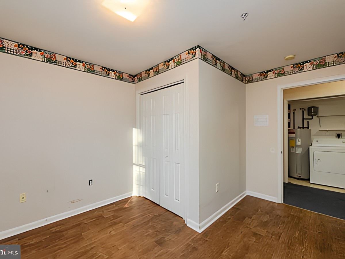 An empty room with hardwood flooring, featuring a closet and a wallpaper border along the ceiling.