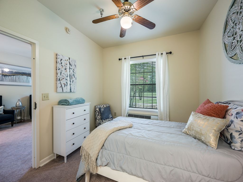 A cozy bedroom with a bed, dresser, and ceiling fan, featuring a window with a view.