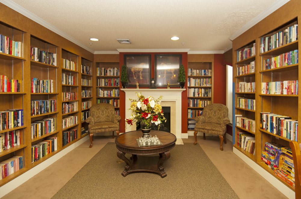 A cozy library with bookshelves lining the walls, a central fireplace, and comfortable seating.