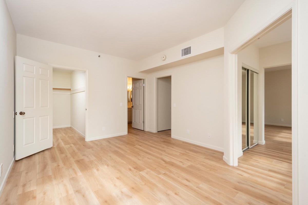 An empty room with wooden flooring and neutral-colored walls, featuring an open layout.