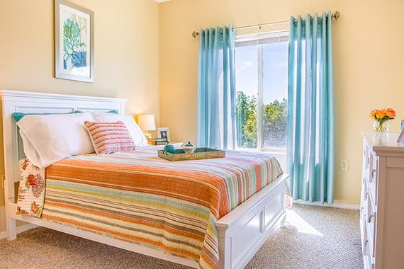 A bright and cozy bedroom with colorful striped bedding and light blue curtains.