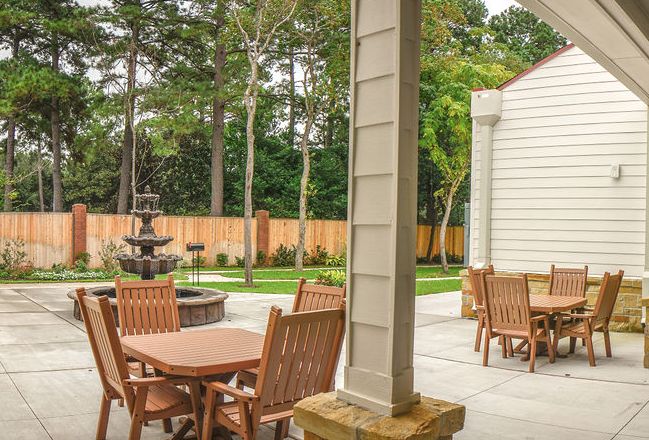 A serene outdoor patio with wooden furniture and a fountain, surrounded by lush landscaping.