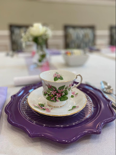 An elegant tea setting featuring a beautifully decorated cup and saucer on a vibrant purple plate, complemented by a delicate floral centerpiece.