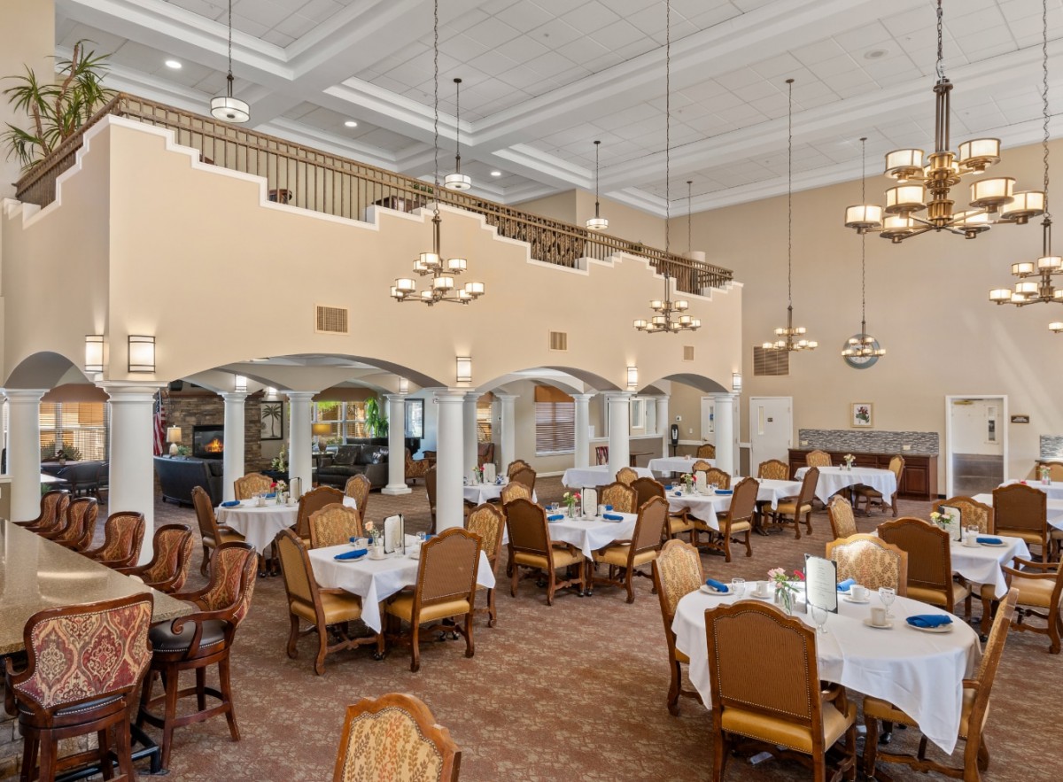 An elegant and spacious dining room with tables set for service, featuring chandeliers and classic decor.