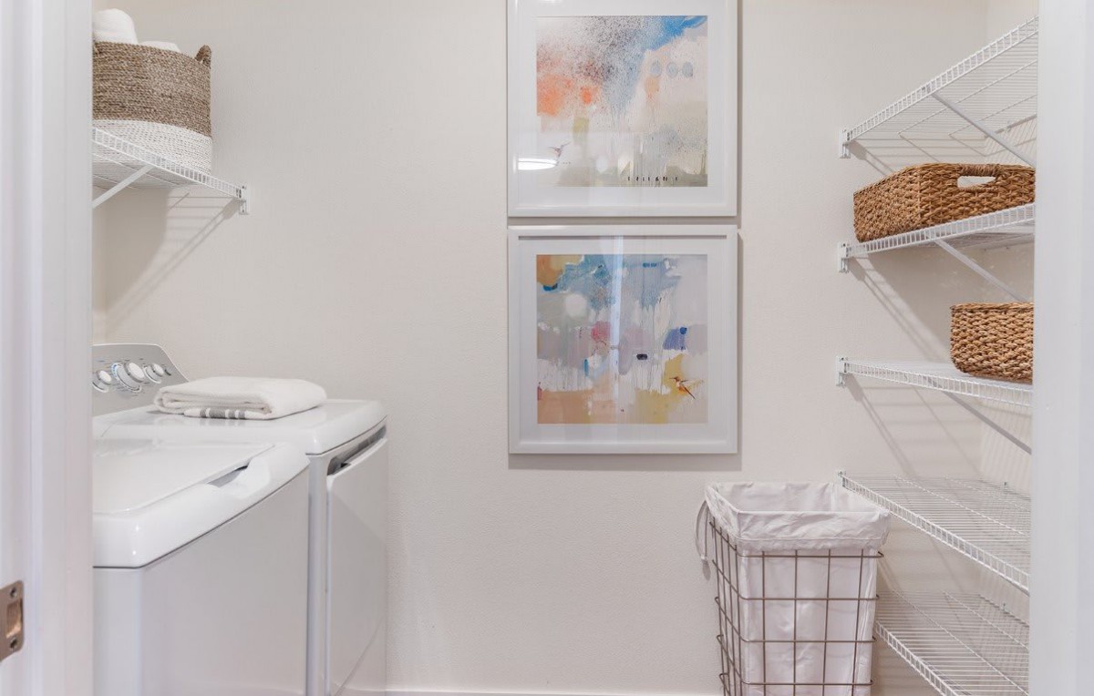 A tidy laundry room with a washer, dryer, and framed artwork on the wall.