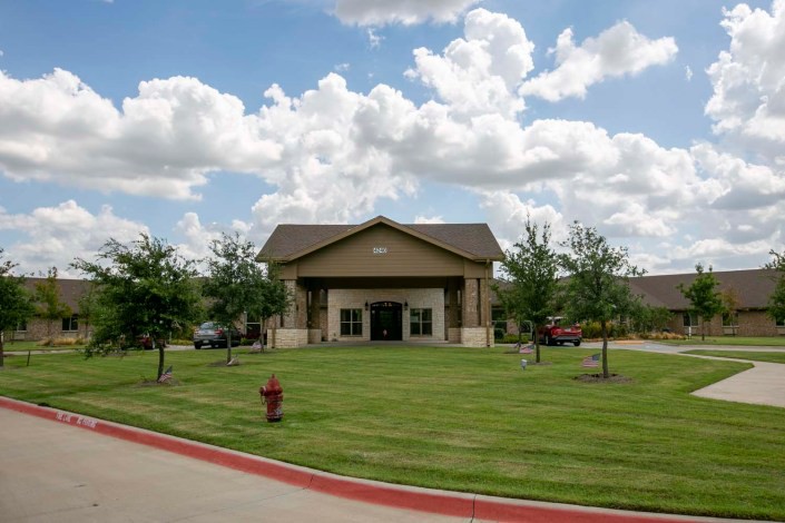 A small building with a well-maintained lawn and trees under a partly cloudy sky.