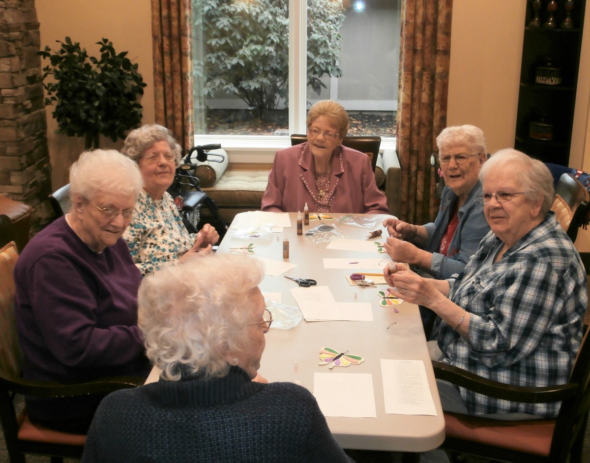 A group of elderly women sitting around a table engaging in activities.