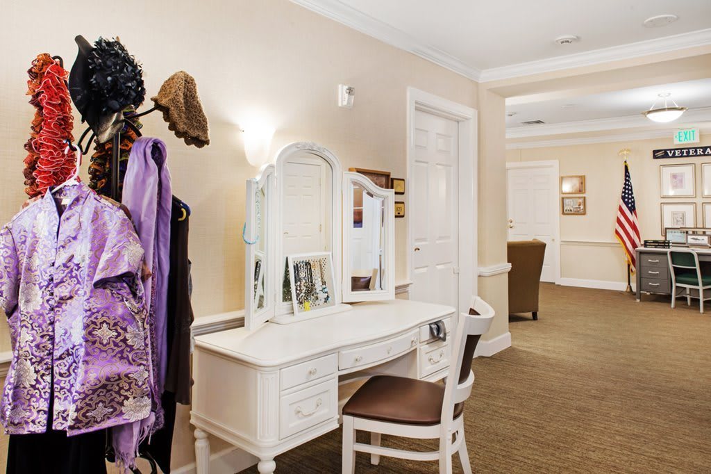 A cozy interior featuring a white vanity with a mirror, accompanied by a chair and personal photographs.