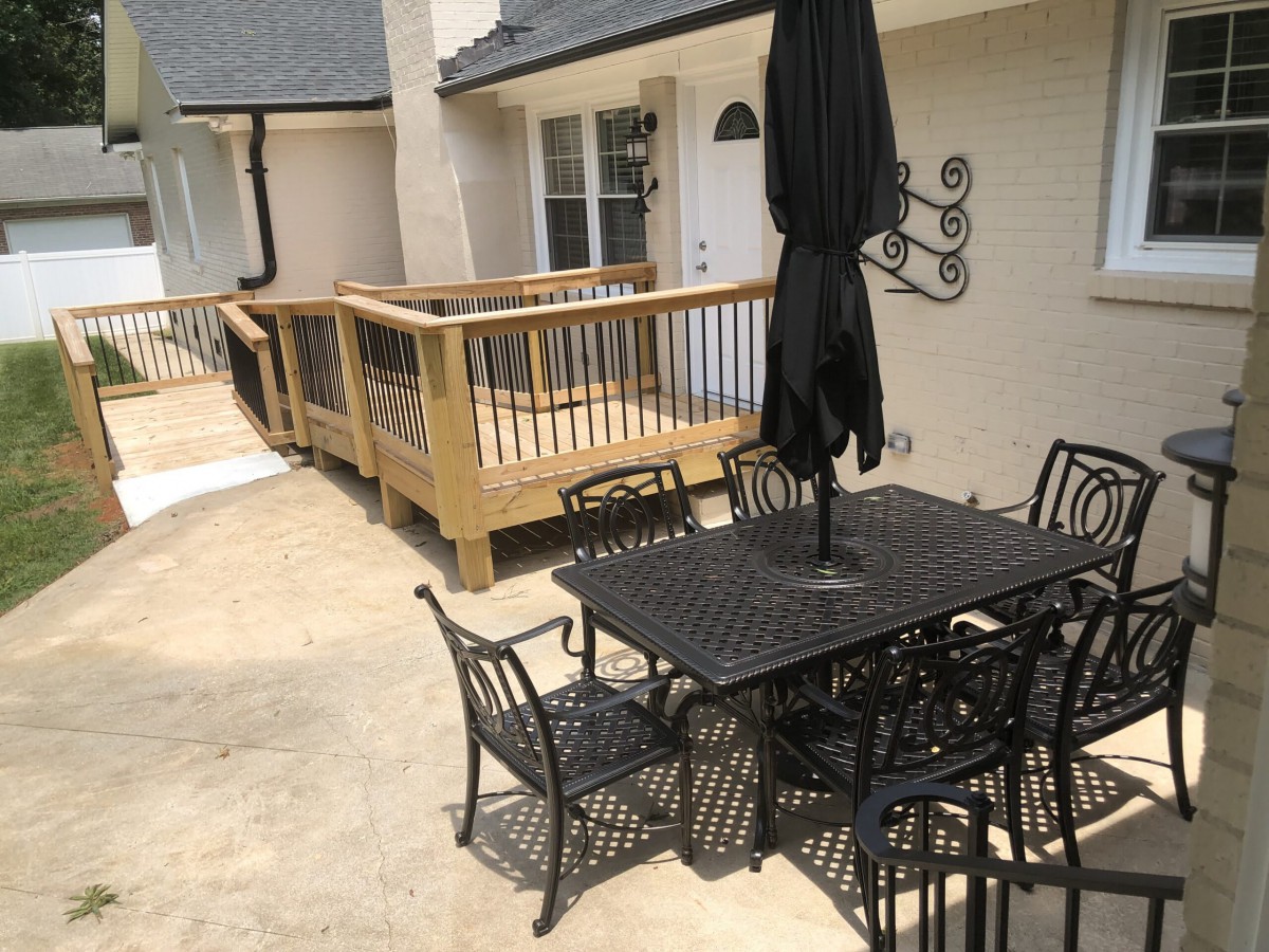 A patio area with a table, chairs, and an umbrella next to a wooden deck.