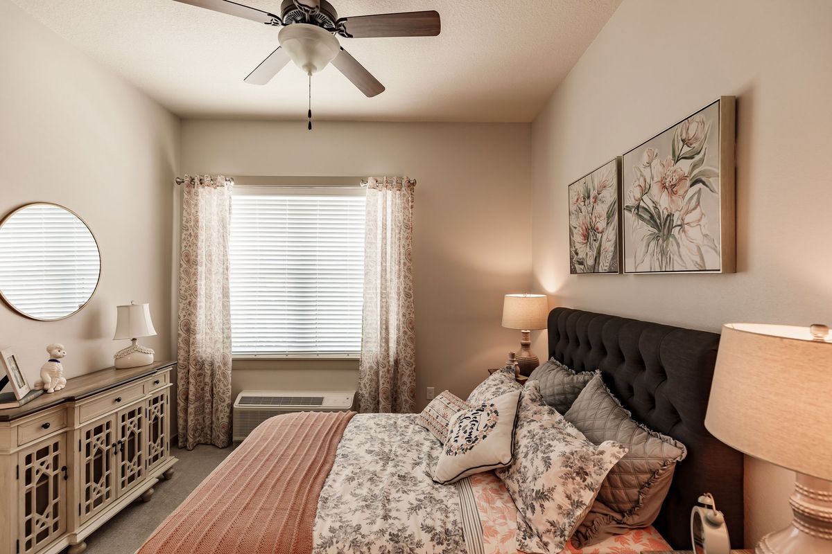 A cozy bedroom with floral bedding, a ceiling fan, and soft lighting.