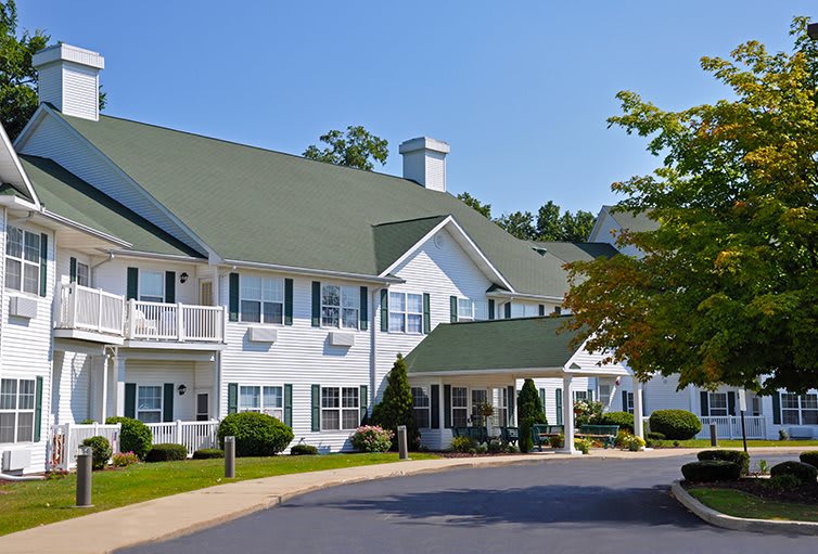 A two-story residential building with a green roof and surrounding trees.