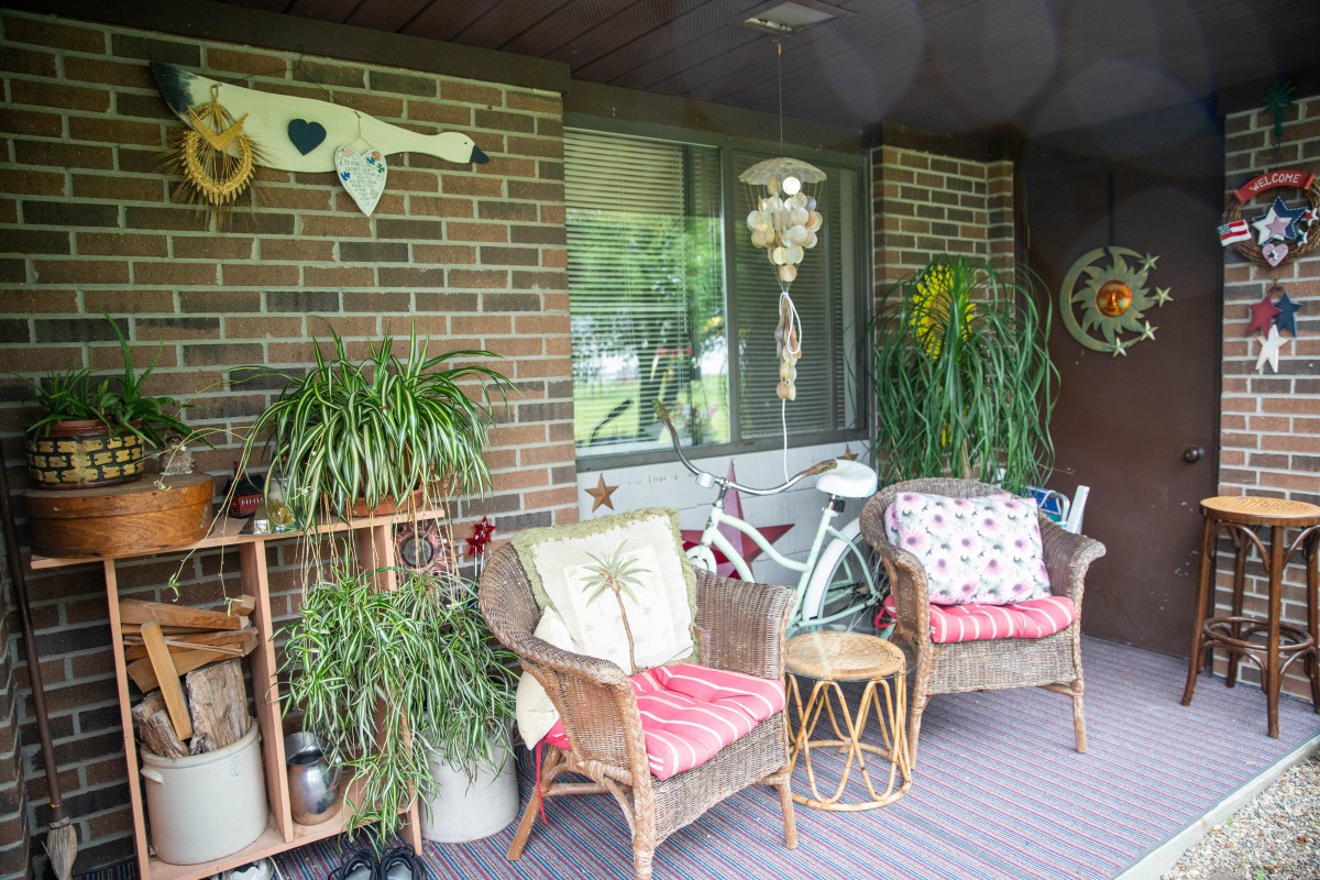 A cozy porch with wicker chairs, vibrant plants, and charming decor against a brick wall.