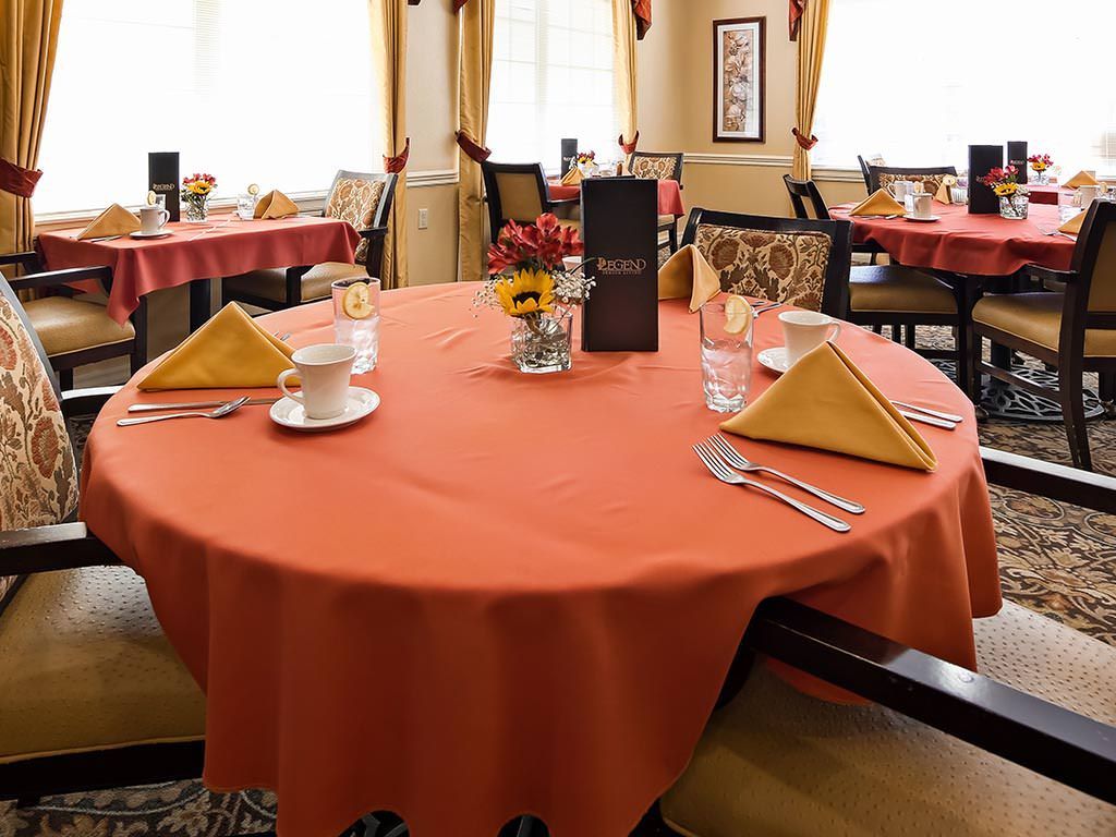 A neatly set dining table in a restaurant with orange tablecloths and folded napkins.