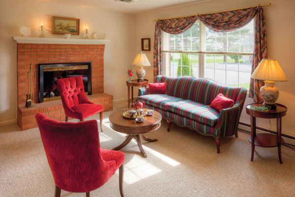 A cozy living room with traditional decor, featuring red chairs, a striped sofa, and a fireplace.