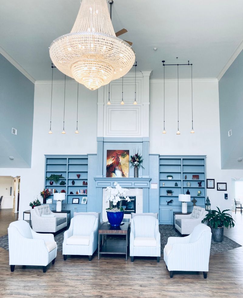 A spacious and elegantly designed living room featuring a grand chandelier, comfortable seating area, built-in bookshelves, and a stylish fireplace with blue and white decor accents.
