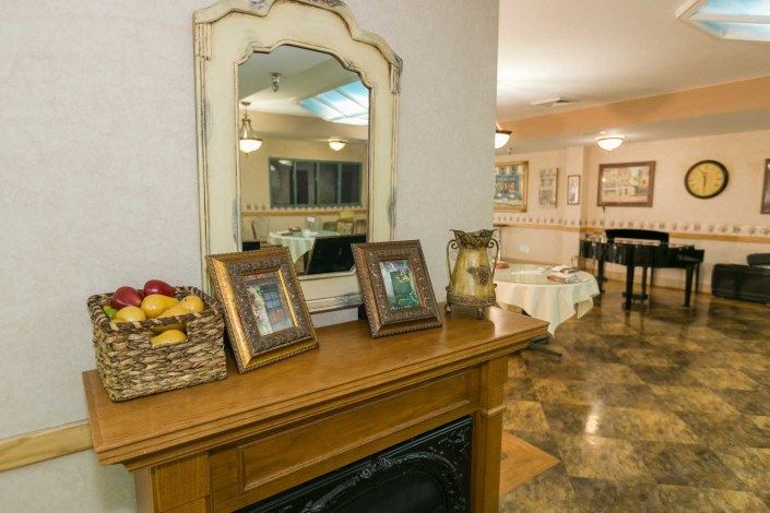 A cozy living room features a wooden mantel with framed photos and a basket of fruit, complemented by a stylish mirror.