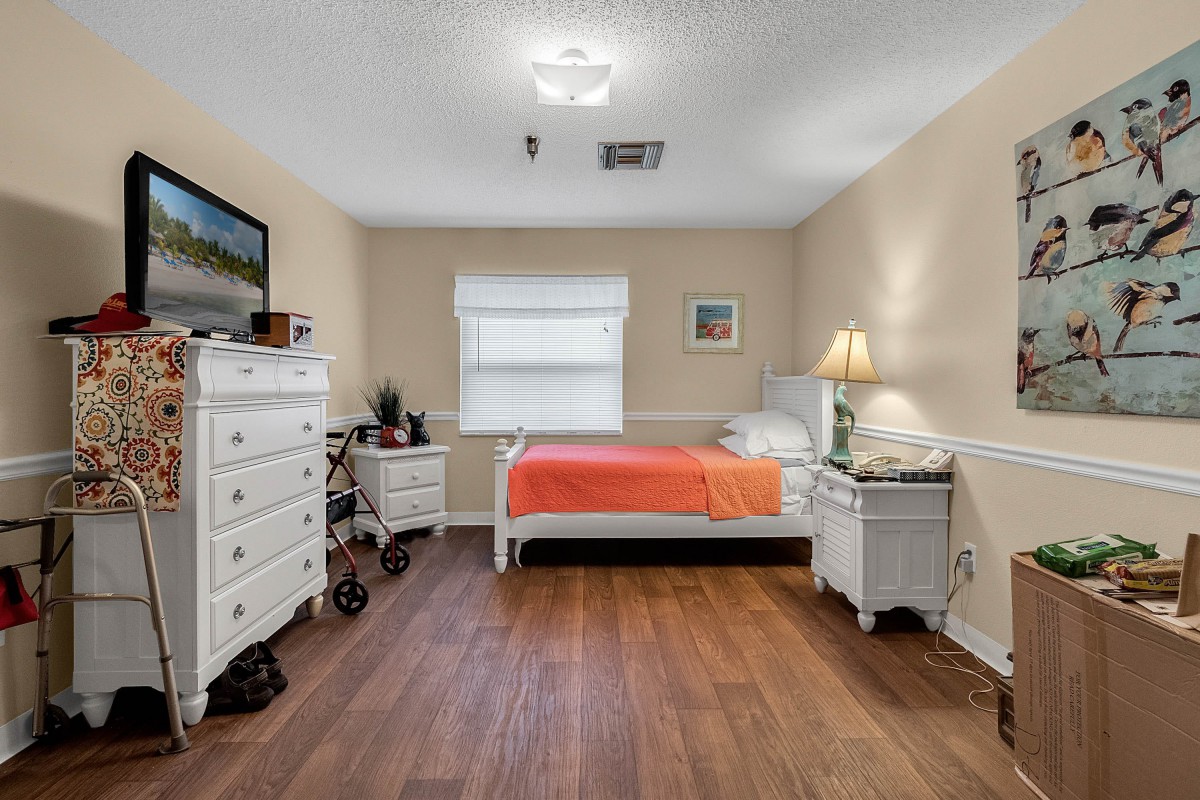 A cozy bedroom with a single bed, dresser, and warm lighting.