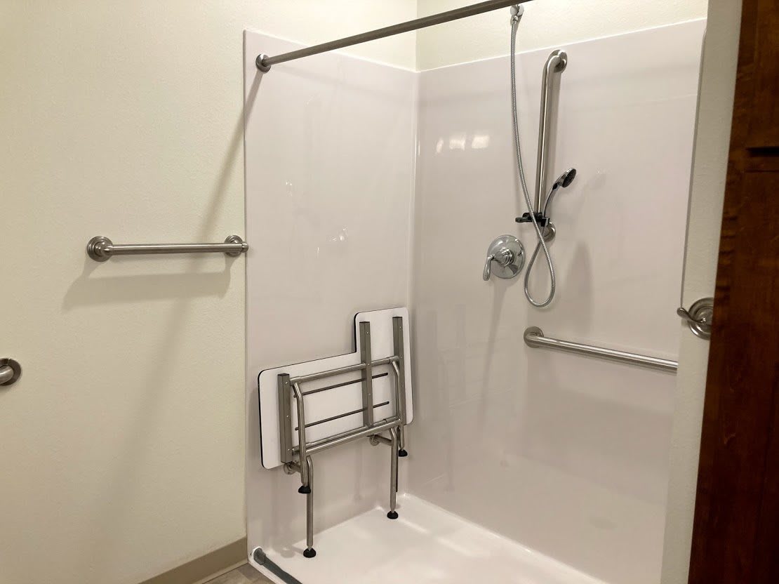 An accessible shower with handrails and a folding seat for support.