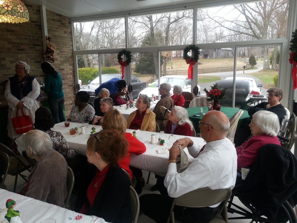 A group of people gathered indoors for a festive holiday celebration, sitting around tables with decorations.