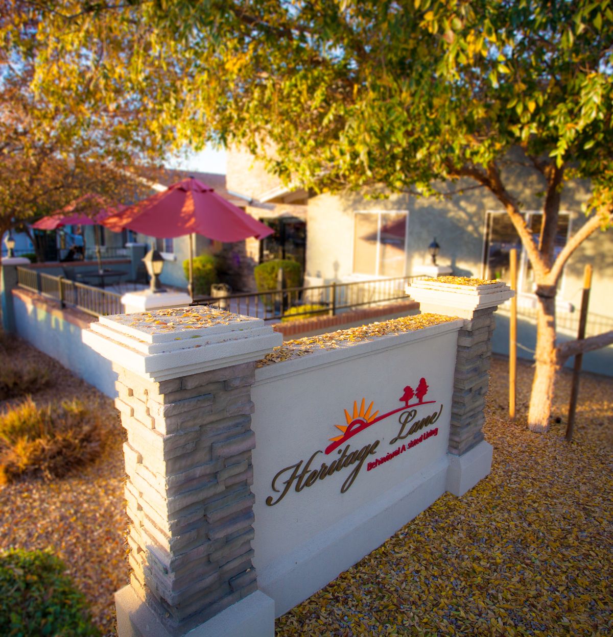 A cozy restaurant with outdoor patio seating shaded by trees, featuring a prominent sign at the entrance.