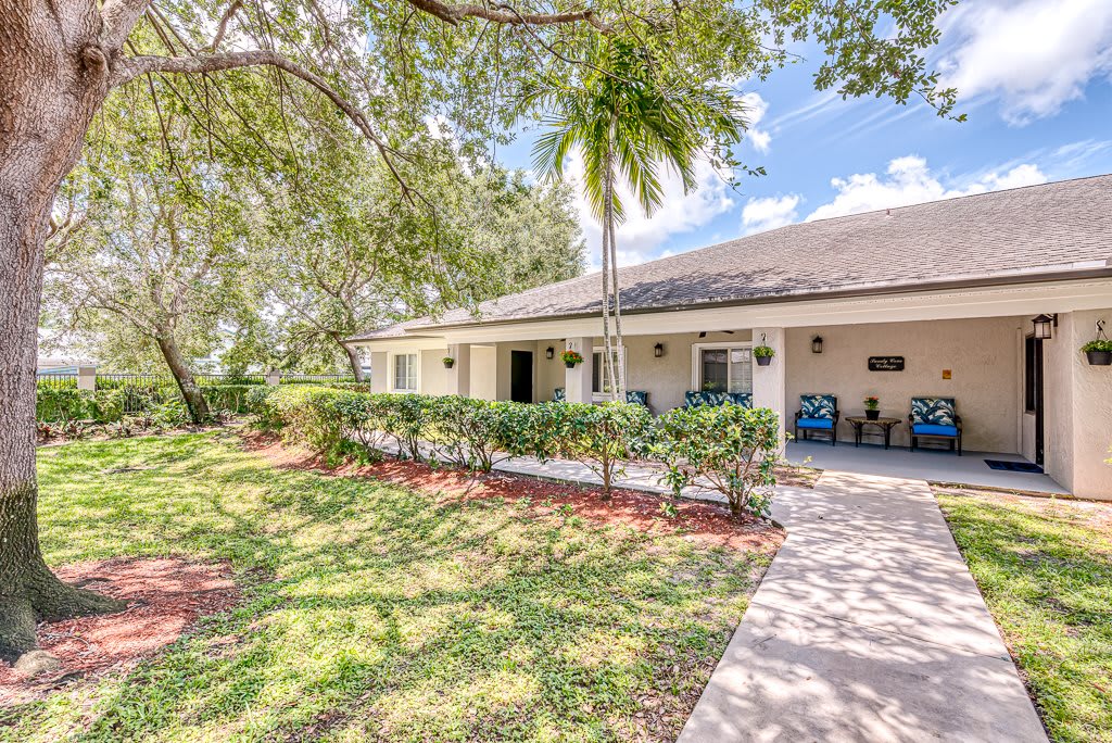 A charming house with a spacious front porch and a well-maintained lawn, surrounded by lush trees on a sunny day.