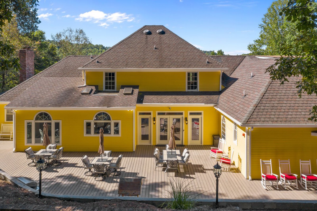 A vibrant yellow house with a spacious backyard patio area, featuring outdoor furniture under a clear, sunny sky.