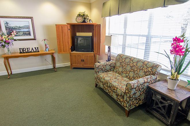 A cozy living room featuring a patterned couch, a wooden TV cabinet, and large windows with natural lighting.
