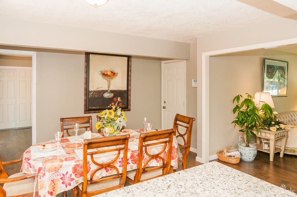 A beautifully decorated dining room with a floral tablecloth, elegant chairs, and artwork on the wall.