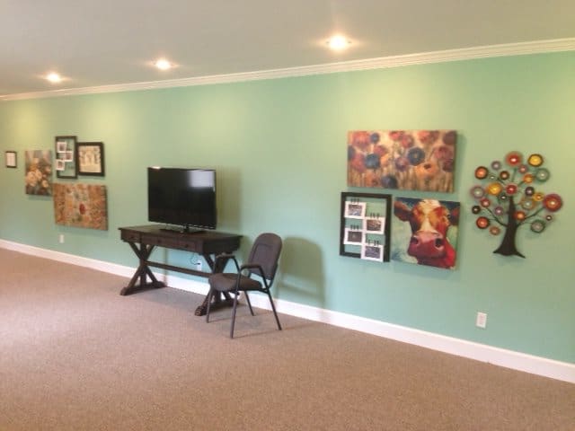 A living room with a green wall decorated with various artworks, a television on a stand, and a chair.