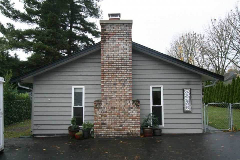 A house exterior with a central brick chimney and two windows on either side.