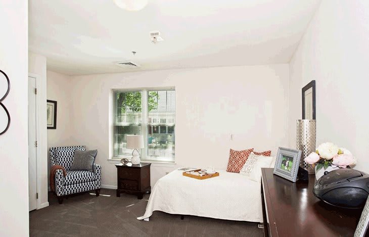 A cozy bedroom with a single bed, a striped armchair, and a large window.