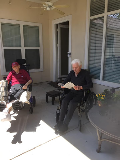 Two elderly individuals enjoying a sunny day on the patio, one reading a book.