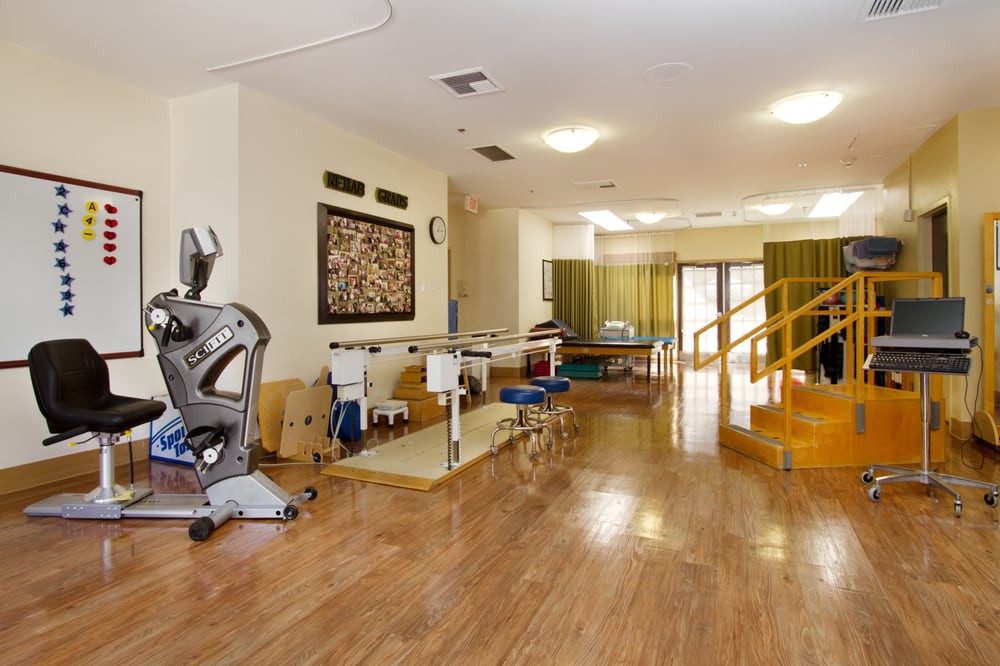 A spacious rehabilitation and physical therapy room equipped with exercise machines and therapy tables.