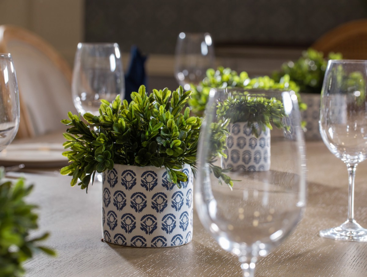 A well-decorated table with wine glasses and a potted plant centerpiece.