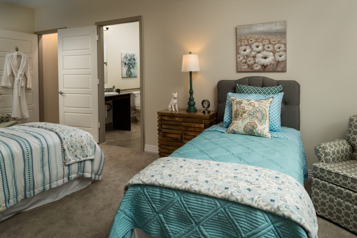 A cozy bedroom with two twin beds featuring turquoise bedding and a nightstand with a lamp.