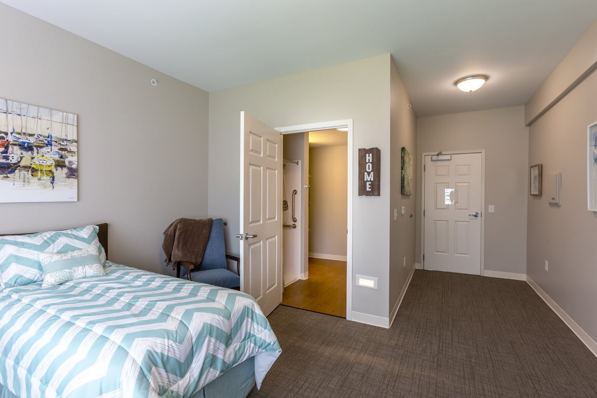 A cozy bedroom interior with a bed, chair, and open doorway leading to the hallway.