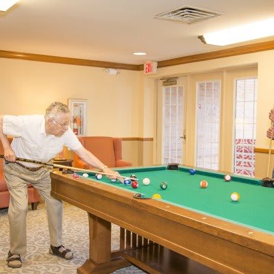 An elderly person playing pool in a cozy game room.