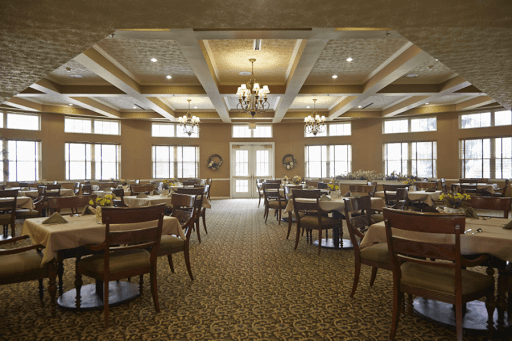 An elegant dining room with neatly arranged tables and chairs, featuring large windows and warm lighting.