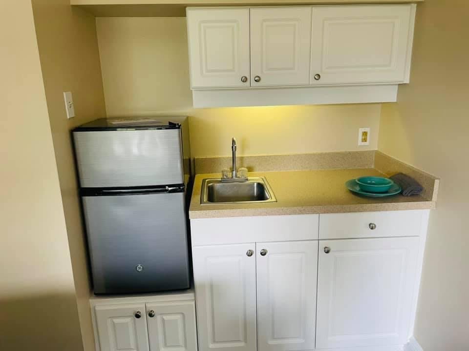 A compact kitchenette with a mini fridge, sink, and white cabinets.