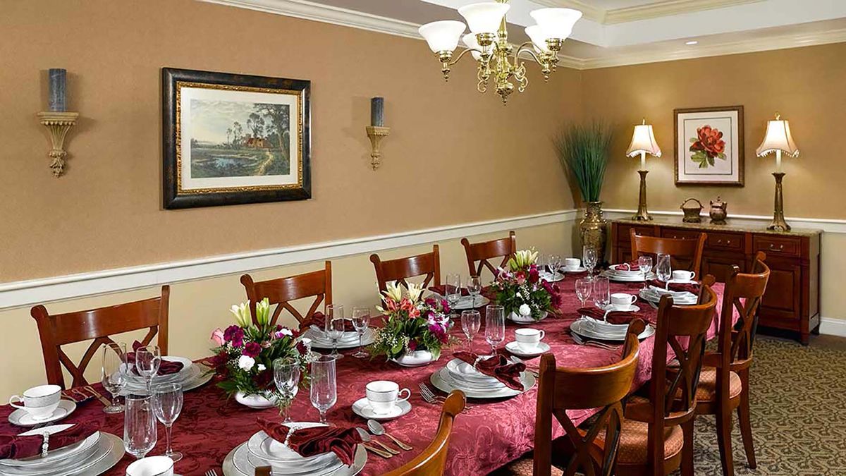 A formal dining room with a long table set for a meal, featuring elegant tableware and floral centerpieces.