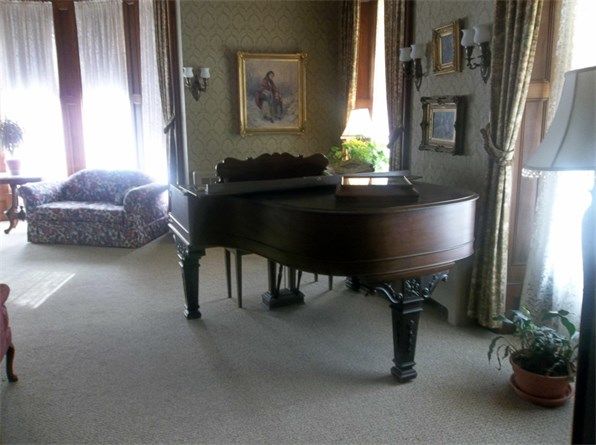 A grand piano in a warmly decorated living room with various framed artworks on the walls.