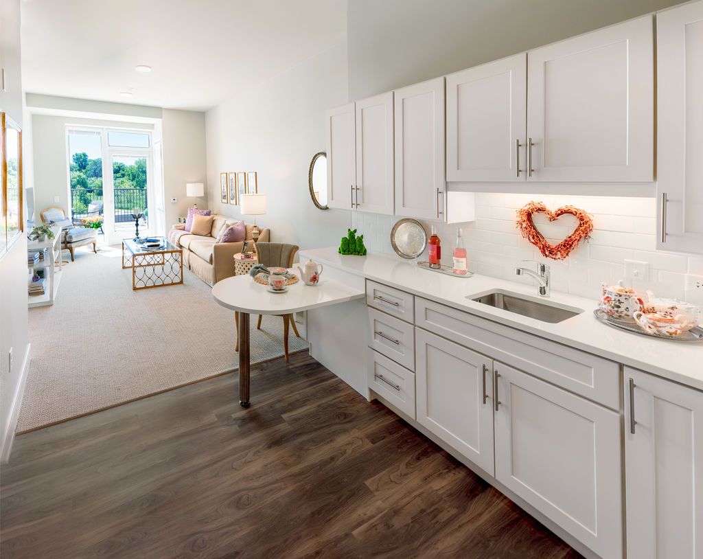 A modern kitchen with white cabinets and a cozy living area, featuring wood flooring and tasteful decorations.