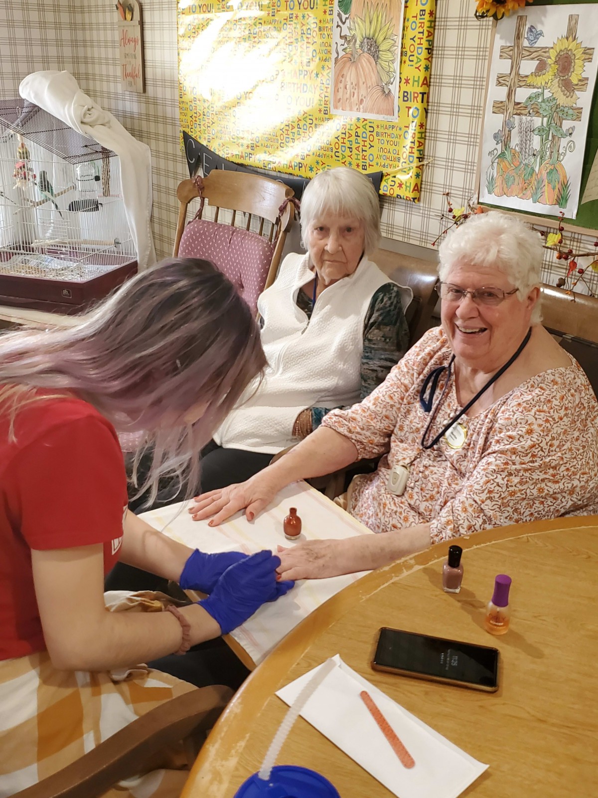 A young woman gives a manicure to two elderly women, bringing smiles and joy.